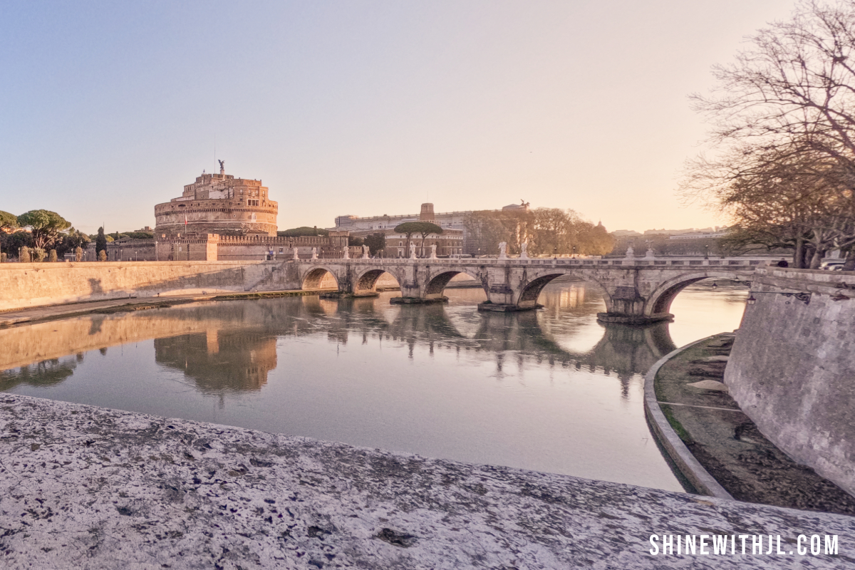 Landscape photo of Castel Sant’Angelo at sunrise with golden light and empty cobblestone streets in Rome